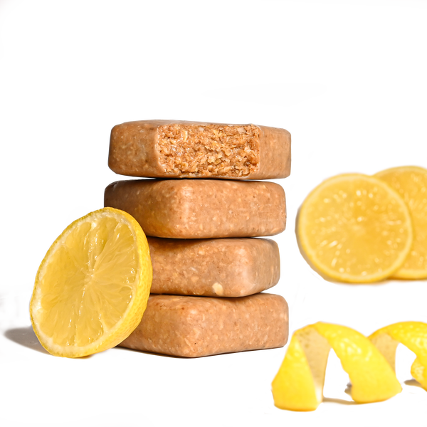 Stack of Performance² Dual-Carb & Electrolyte Energy Bars with lemon slices and a squeezed lemon on a white background.