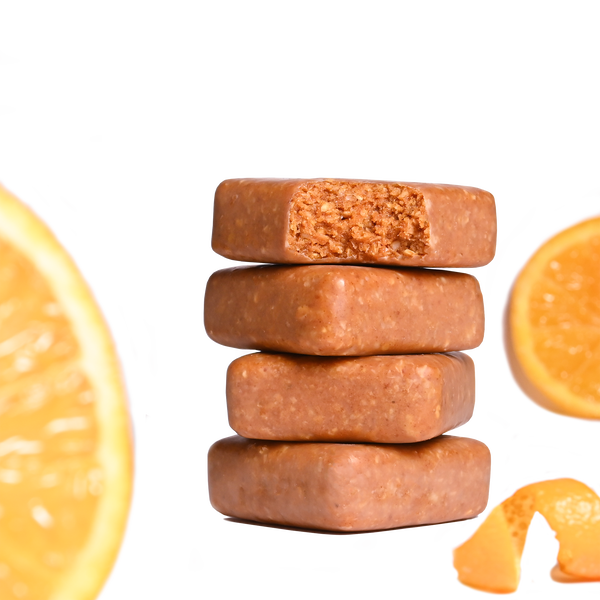 Stack of Performance² Dual-Carb & Electrolyte Energy Bars with orange slices and an orange zest on a white background.